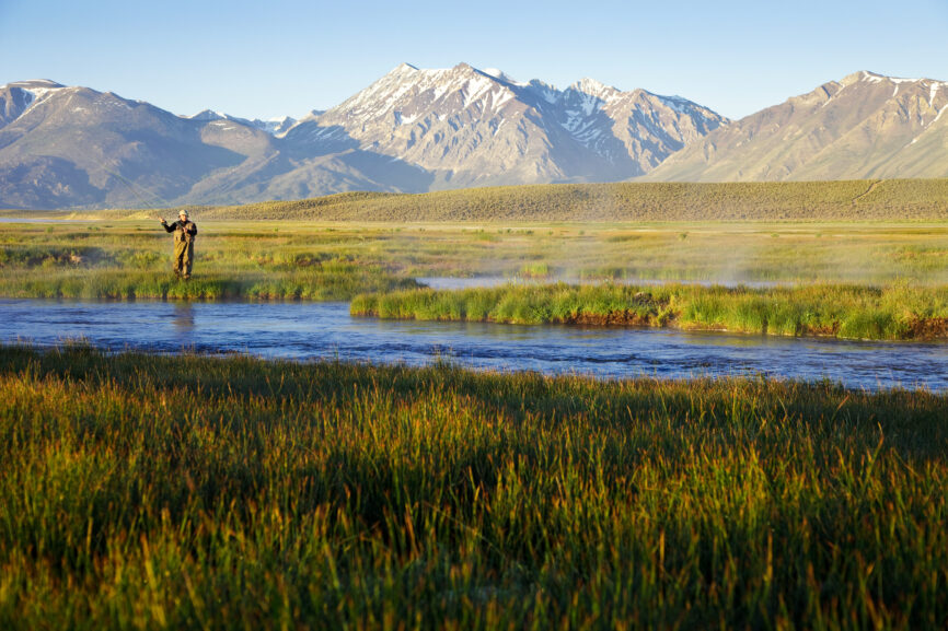 One man fly fishing on the Owens River at sunrise with the Sierra Nevada Mountains in distance