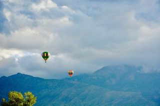 Multiple airship balloons in the air above the mountains