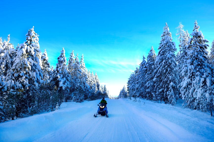 Snowmobiling on snowy mountain road with snow covered pine trees wilderness