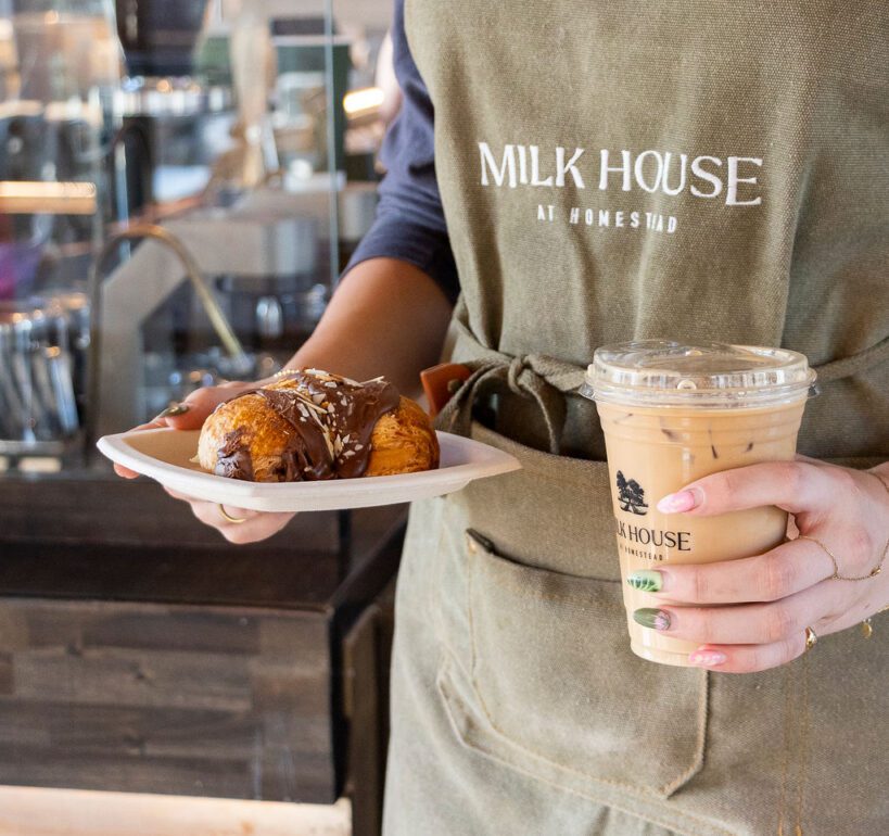 Milkhouse staff member is holding pastry and cold brew