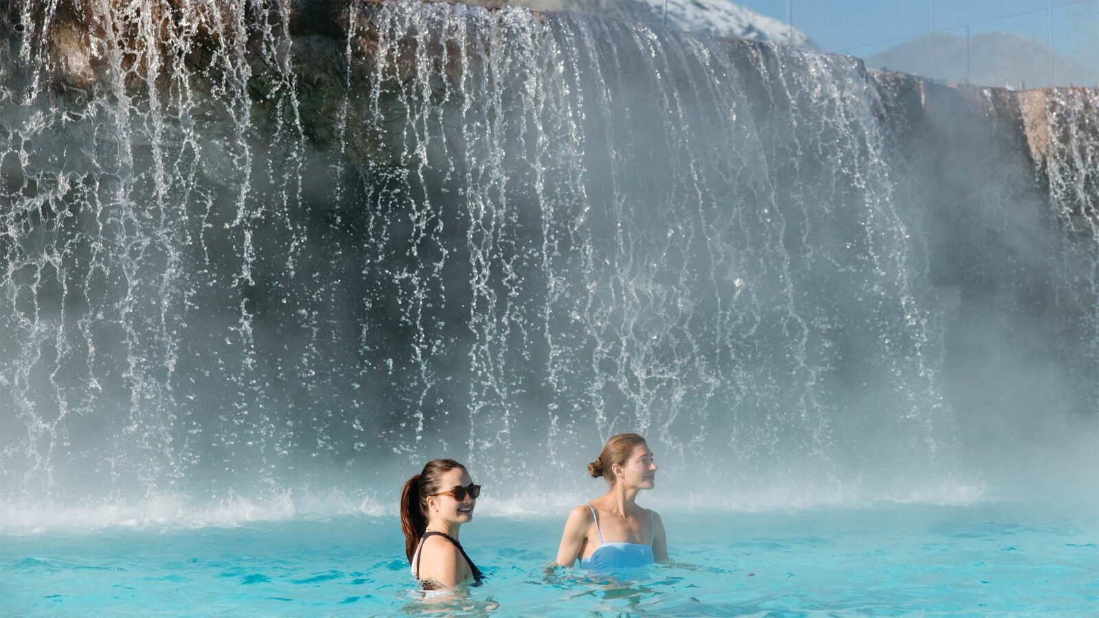 Two People Enjoying the Waterfall Feature at The Pools at Homestead