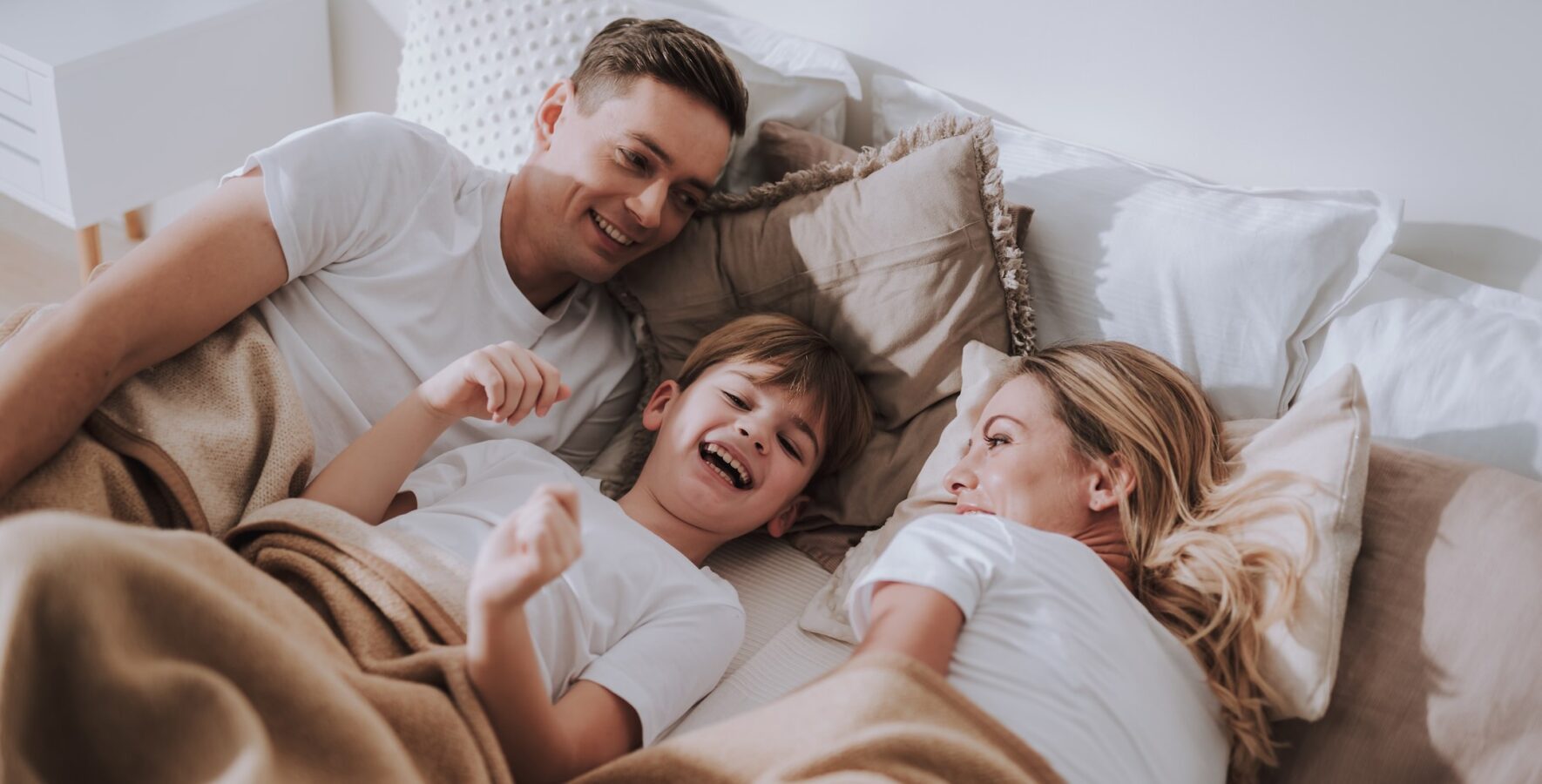 Special offers at Homestead. Family lying in bed laughing together.