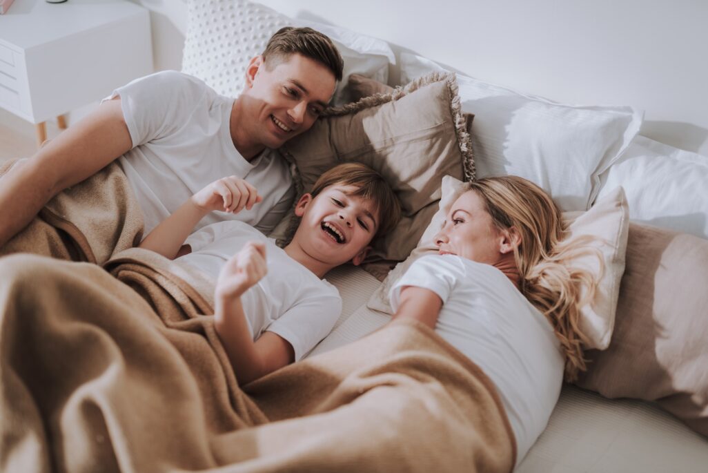 Special offers at Homestead. Family lying in bed laughing together.